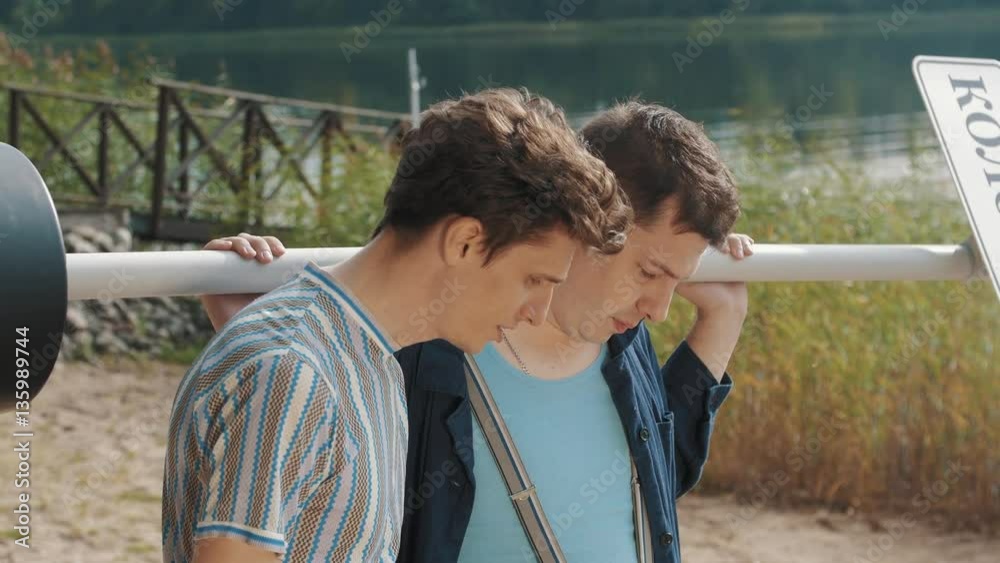 Two guys stand on sandy shore looking down, talking and start yelling on a summer day Two guys stand on sandy shore looking down, talking and start yelling on a summer day