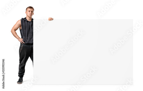 Muscular young man in sportswear is holding a side of a huge blank banner isolated on white background © gearstd