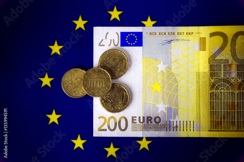 European  cash money. Two hundred euro bill lying on the European community flag. Four twenty euro cents coins on the  bill. Macro image. Dark background. photo