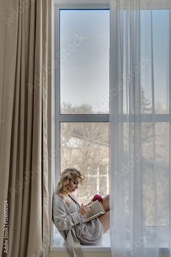 Girl sitting on a window sill reading a book
