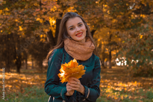 cute girl in a warm scarf holds the leaves looks straight and smiling