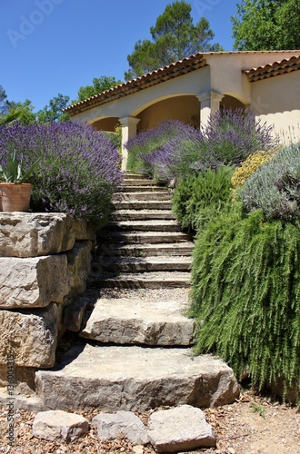 Entrance to french summerhouse surrounded by stone wall, lavender and rosemary flowerbed