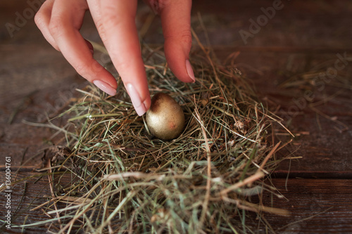 Putting one golden egg into straw nest closeup. Woman preparing for Easter, handmade decoration of house. Tradition, family, spring, investments, Bank deposit concept