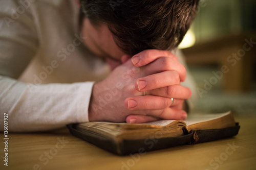 Fotografie Unrecognizable man praying, kneeling on the floor, hands on Bibl