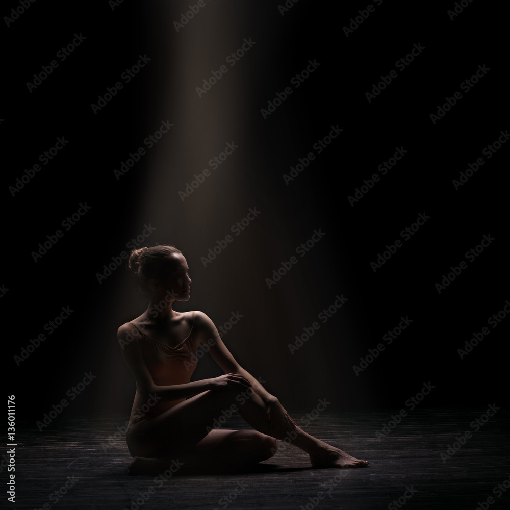 silhouette of beautiful woman ballet dancer sitting on wooden floor over dark background