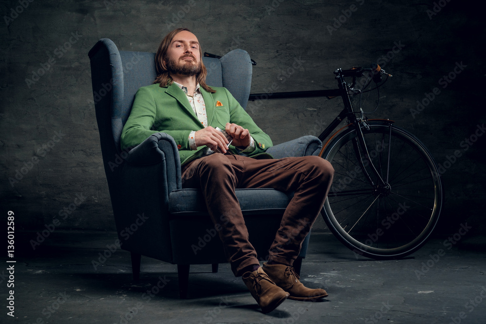 A man sits on a chair with bicycle on background.