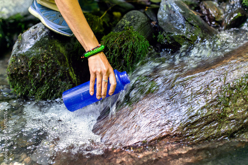 beautiful woman taking water from forest spring on hiking trip