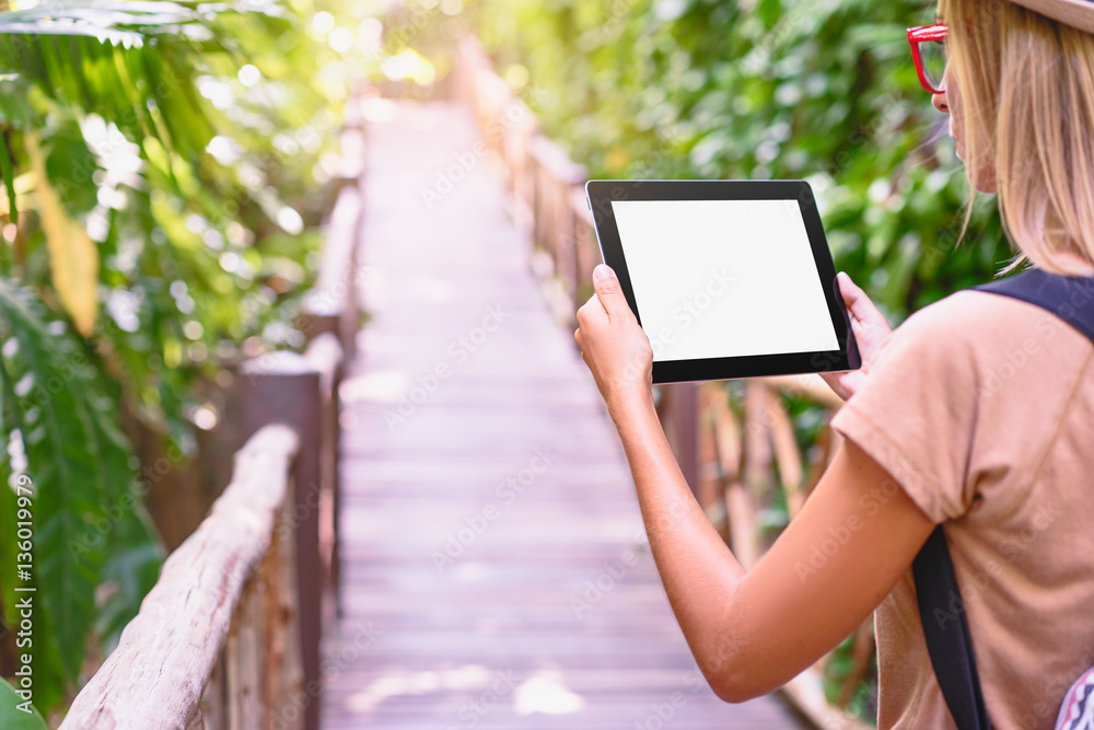 Traveling concept. Technology and adventure. Young woman using tablet computer in jungle.