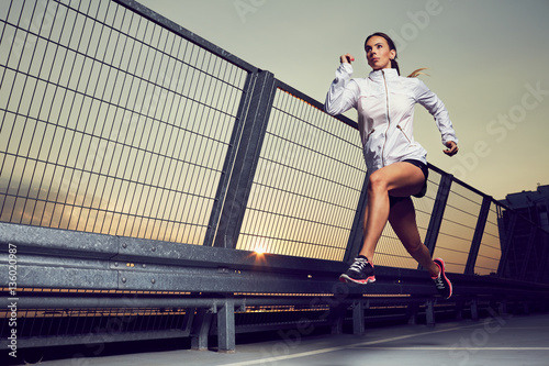 Foto Athletic woman running during sunset on rooftop of parking, garage