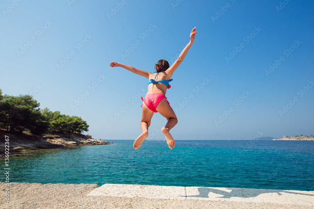 Child little girl is jumping into the sea from a pier