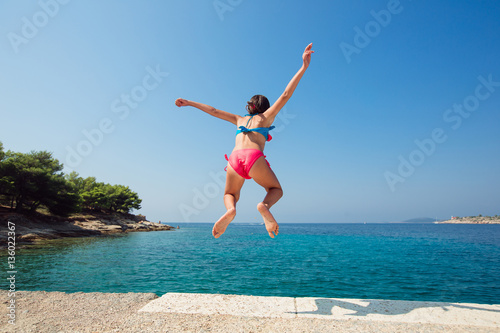Child little girl is jumping into the sea from a pier