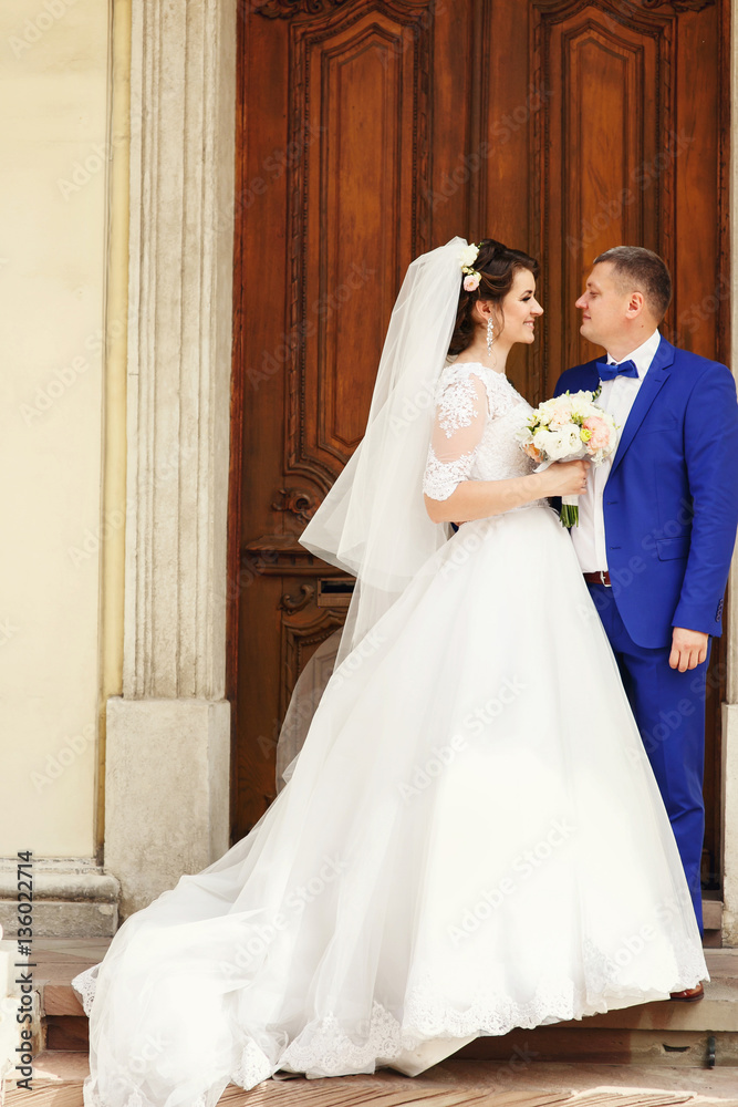 Bride in magnificent dress and groom in blue suit look at each o Bride in magnificent dress and groom in blue suit look at each o