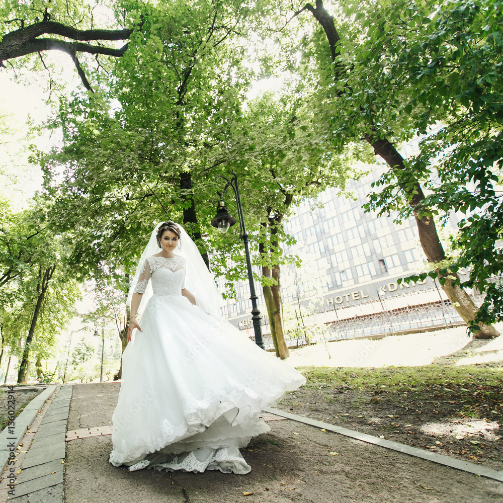 Bride raises her dress while she whirls on path in park Bride raises her dress while she whirls on path in park