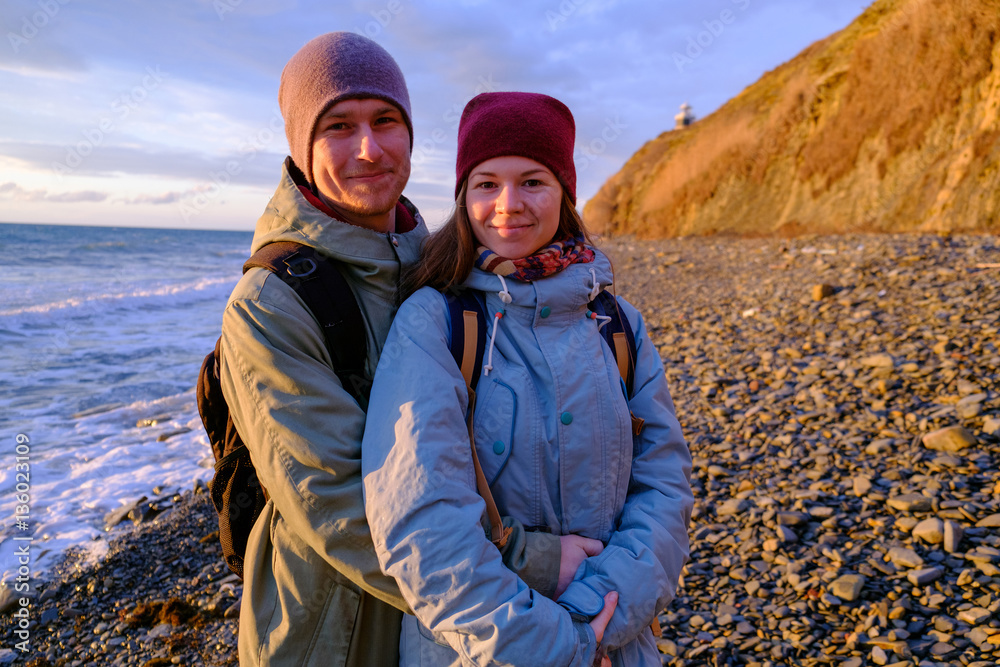 young couple hugging on seashore near cliff during sunrise