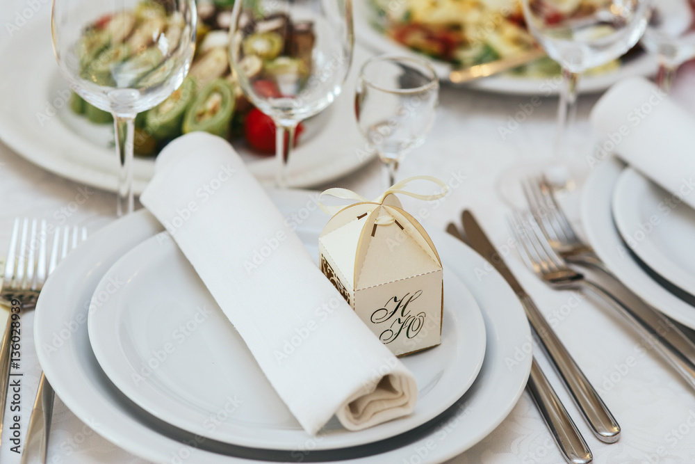 Little box with present stans behind the roll of serviette on dinner plate Little box with present stans behind the roll of serviette on dinner plate