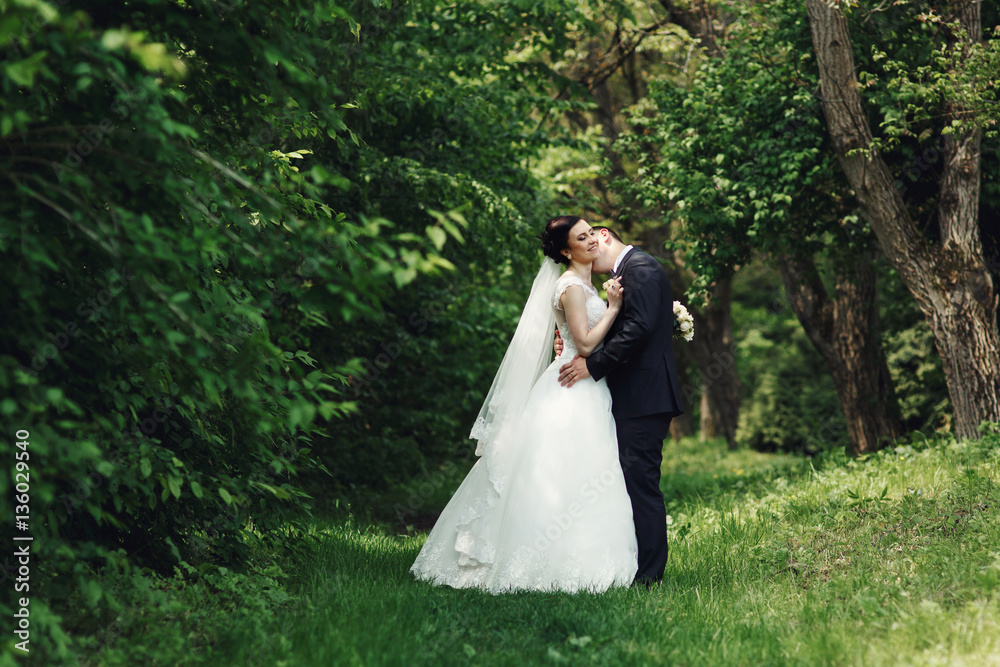 Groom kisses bride's neck while they stand in the forest