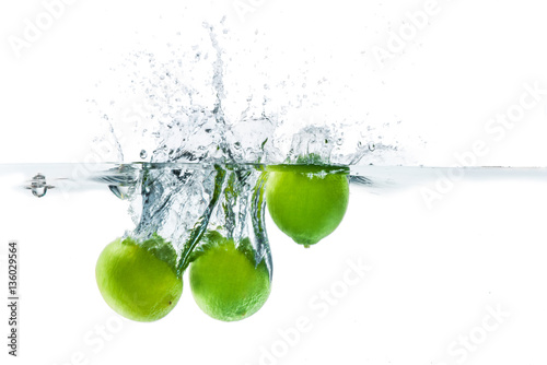 Fresh lime dropped into the water with water splash on a white b