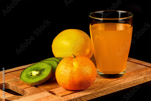 Mandarin, kiwi, lemon and glass of juice on a black background close-up.