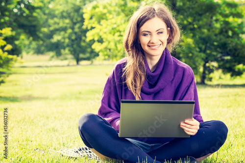 Young woman using laptop in the park sitting on the green grass