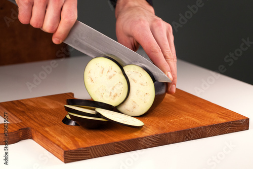Sharp knife cutting egplant into slices. Nice wooden cutting board. Dieting concept photo