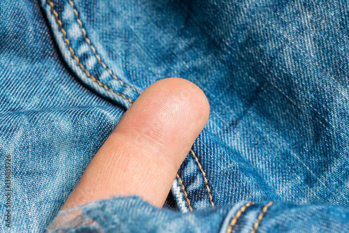 Human finger sticks out from a hole in jeans