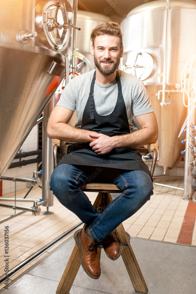Full body portrait of handsome brewer sitting on the chair at the beer manufacturing Full body portrait of handsome brewer sitting on the chair at the beer manufacturing