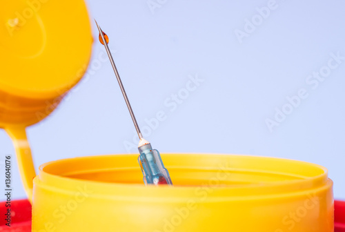 Yellow medical disposal waste box, syringe needle with red drop on the tip