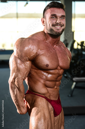Brutal strong bodybuilder man pumping up muscles and train gym