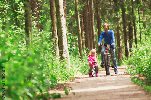 family sport - father and daughter riding bikes in green forest