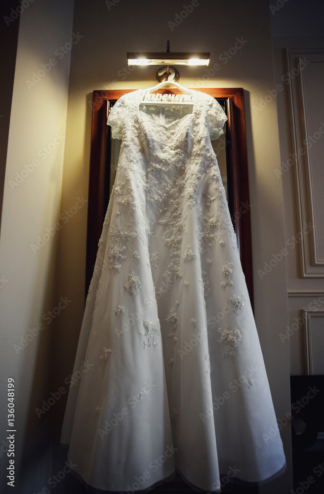 The wedding dress hangs near mirror