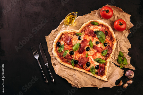 Pizza heart love Valentine's Day romantic Italian restaurant dinner food. Prosciutto, olives, tomatoes, parsley, basil and mozzarella cheese meal on black