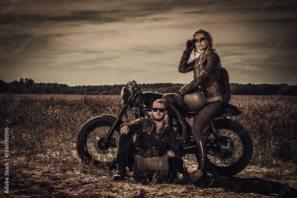 Fototapeta premium Young, stylish cafe racer couple on vintage custom motorcycles in field