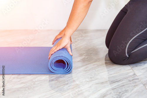 Close-up of attractive young woman folding blue yoga or fitness mat after working out at home in living room. Healthy life, keep fit concepts.