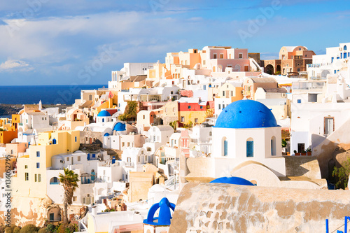 View of the seaside on a summer day. .Numerous white cottages cover the high seashore on the background of blue water..Panorama of Oia village with colorful houses 
