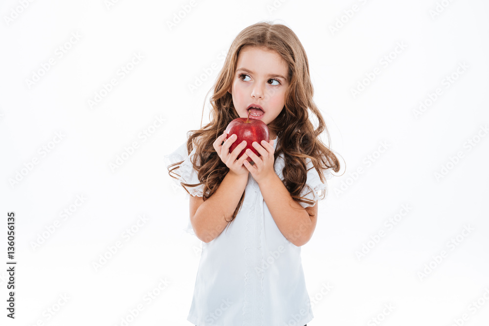 Pensive worried little girl standing and holding red apple
