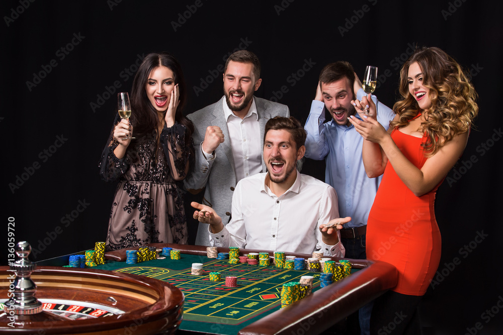 Group of young people behind roulette table on black background Group of young people behind roulette table on black background
