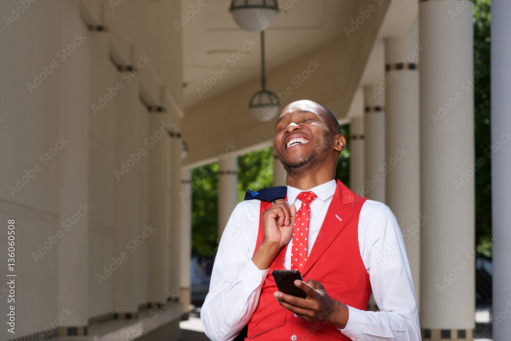 handsome young african man in suit laughing outdoors with cellphone