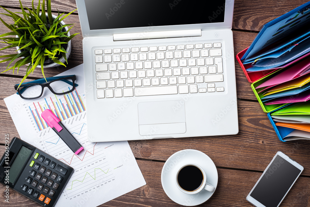 Overhead shot of office desktop with modern computer, graphs and charts, documents and smart phone Overhead shot of office desktop with modern computer, graphs and charts, documents and smart phone