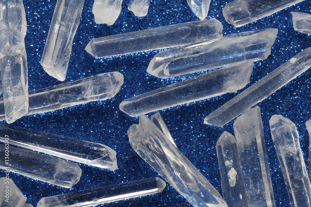 Terminated clear crystal quartz wands - a random scattered selection of clear mini terminated quartz wands on a speckled blue background Terminated clear crystal quartz wands - a random scattered selection of clear mini terminated quartz wands on a speckled blue background