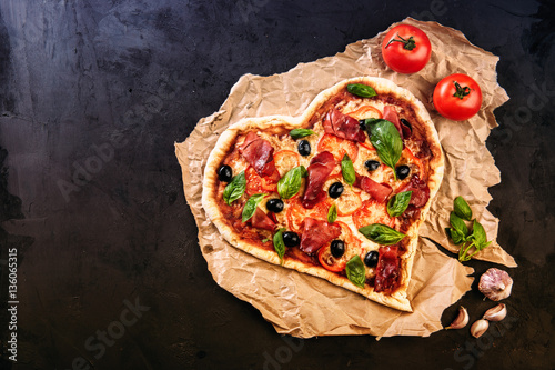 Heart shaped pizza with tomatoes and mozzarella for Valentines Day on vintage black background. Food concept of romantic love
