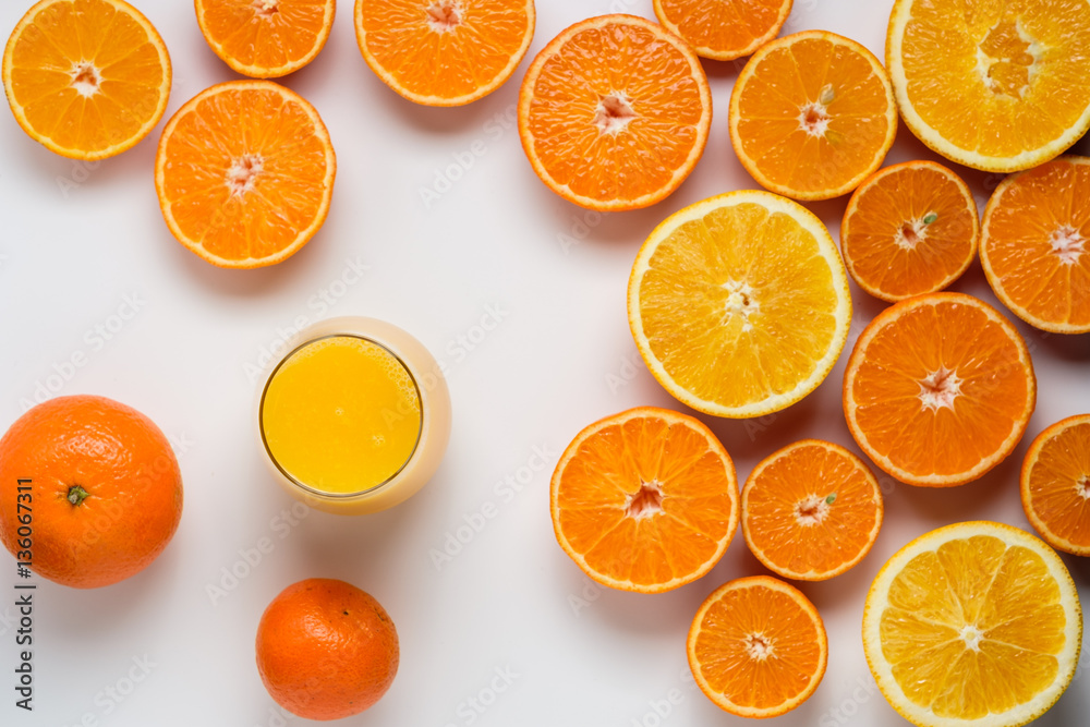 Fototapeta premium A glass of juice and cut oranges and tangerines on a white backg