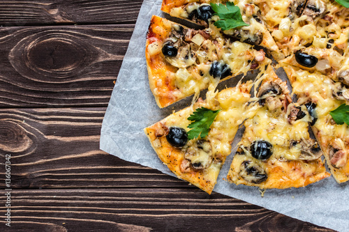Pizza with meat, mushrooms, pineapple and olives on a wooden background
