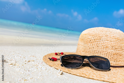 Sun hat and sunglasses on sand, clear turquoise ocean in Maldives.