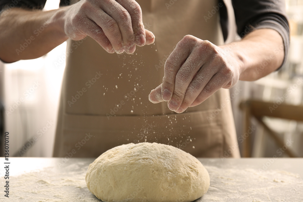 Fototapeta premium Man sprinkling flour over fresh dough on kitchen table