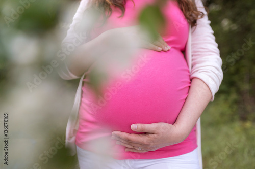 Unrecognizable pregnant women holding her belly. Summer nature.