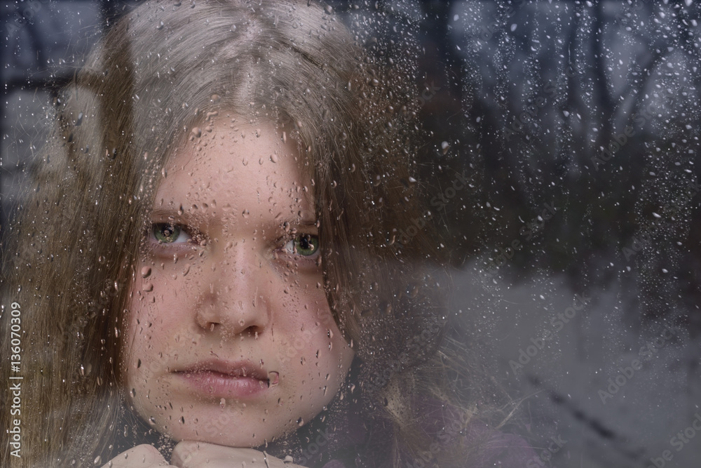 Mädchen blickt durch nasse Fensterscheibe mit Spiegelung Winterlandschaft