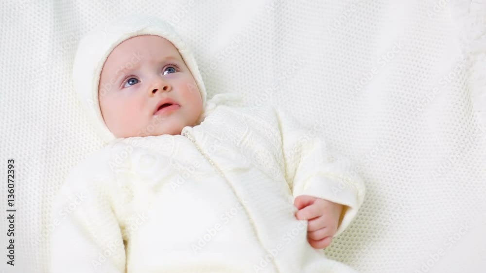baby girl knitted in white overalls lying on the bed baby girl knitted in white overalls lying on the bed