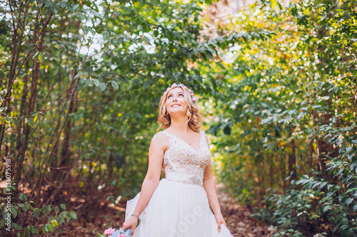 beautiful bride smiling blonde in the forest holding weddg flowers in hands. Wonderland picture.