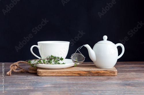 White porcelain tea cup and saucer, thyme herb twig, teapot and