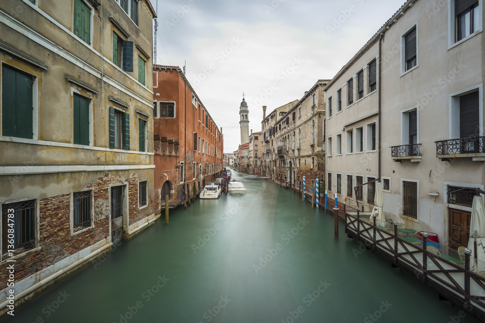 Long time exposure of canal in Venice (Venezia) with old buildings, boats and the leaning belfry tower of San Giorgio dei Greci, Italy, Europe